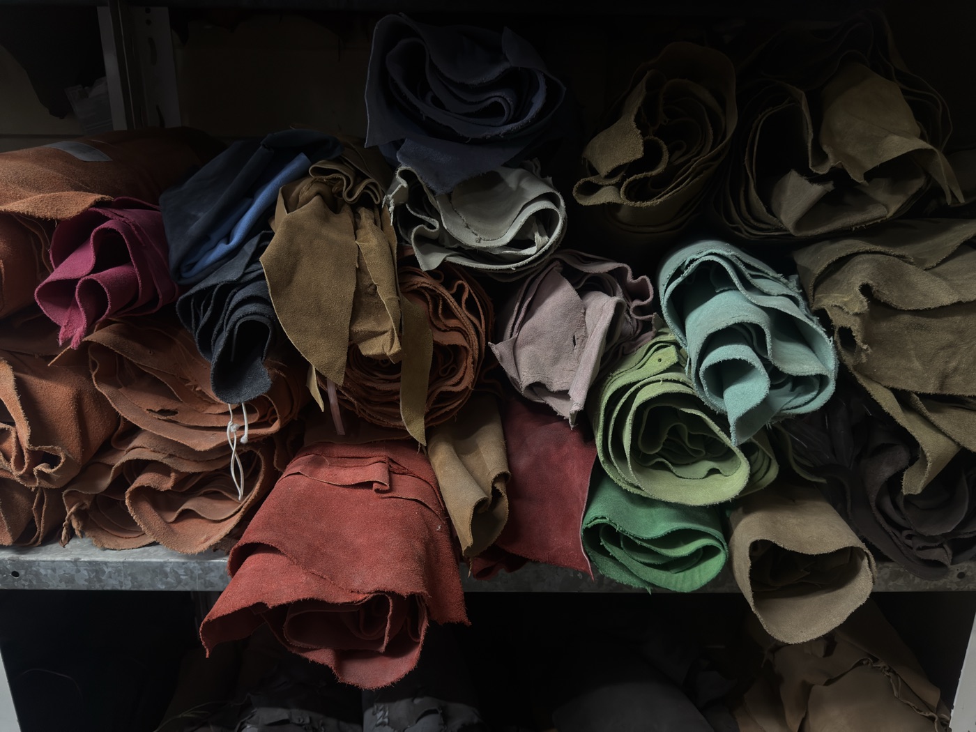 Rolled leather hides in multiple colours on storage shelves at Mac Leather