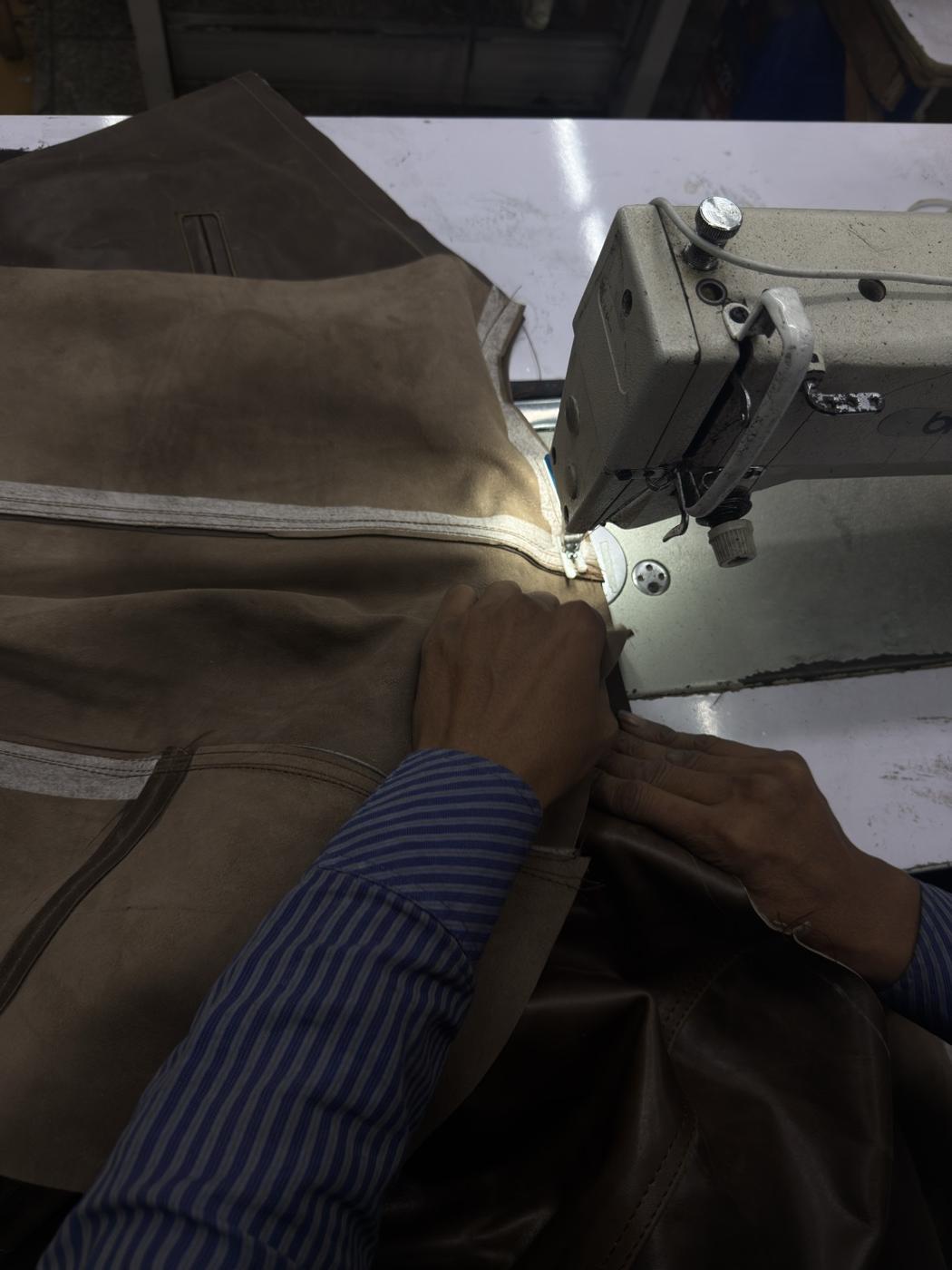 Close-up of leather jacket zipper area being sewn by skilled craftsman