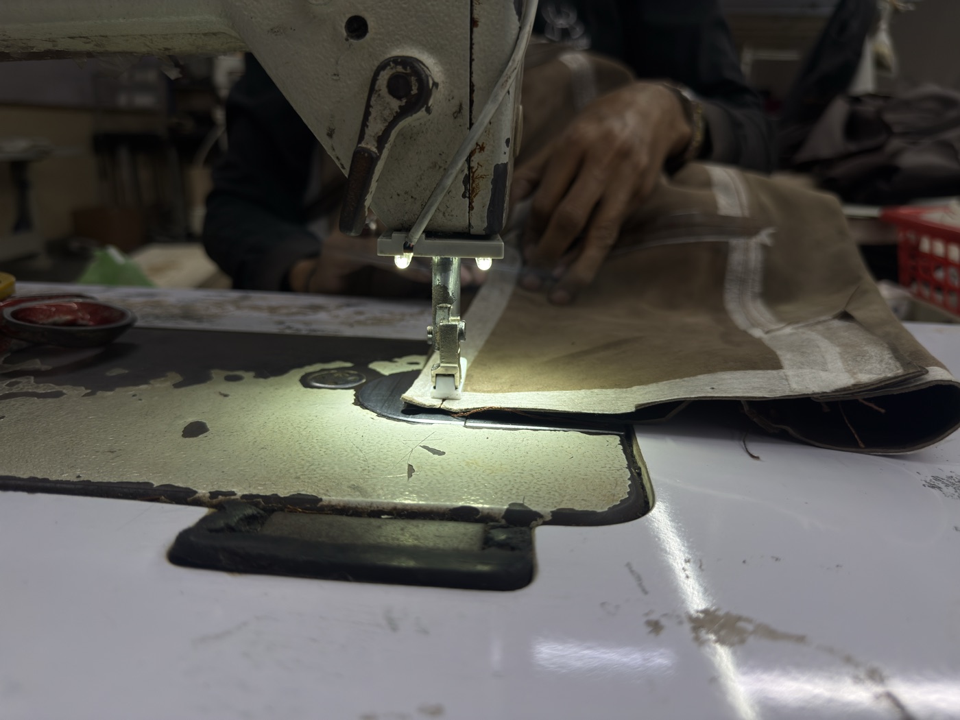 Close-up of tan leather panel being stitched on industrial sewing machine